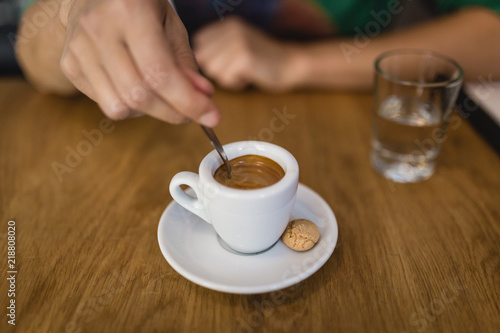 Coffee time: Female hand with teaspoon & espreso cup against wooden table