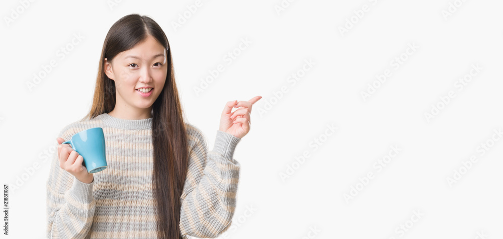 Young Chinese woman over isolated background driking cup of coffee very happy pointing with hand and finger to the side Young Chinese woman over isolated background driking cup of coffee very happy pointing with hand and finger to the side