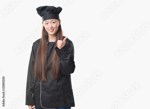 Young Chinese woman over isolated background wearing chef uniform doing happy thumbs up gesture with hand. Approving expression looking at the camera with showing success.