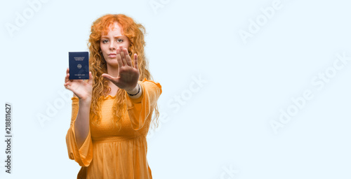 Young redhead woman holding passport of Germany with open hand doing stop sign with serious and confident expression, defense gesture