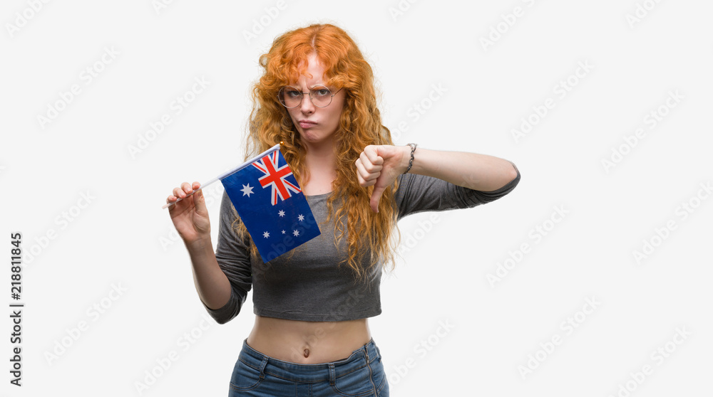 Young redhead woman holding flag of Australia with angry face, negative sign showing dislike with thumbs down, rejection concept Young redhead woman holding flag of Australia with angry face, negative sign showing dislike with thumbs down, rejection concept
