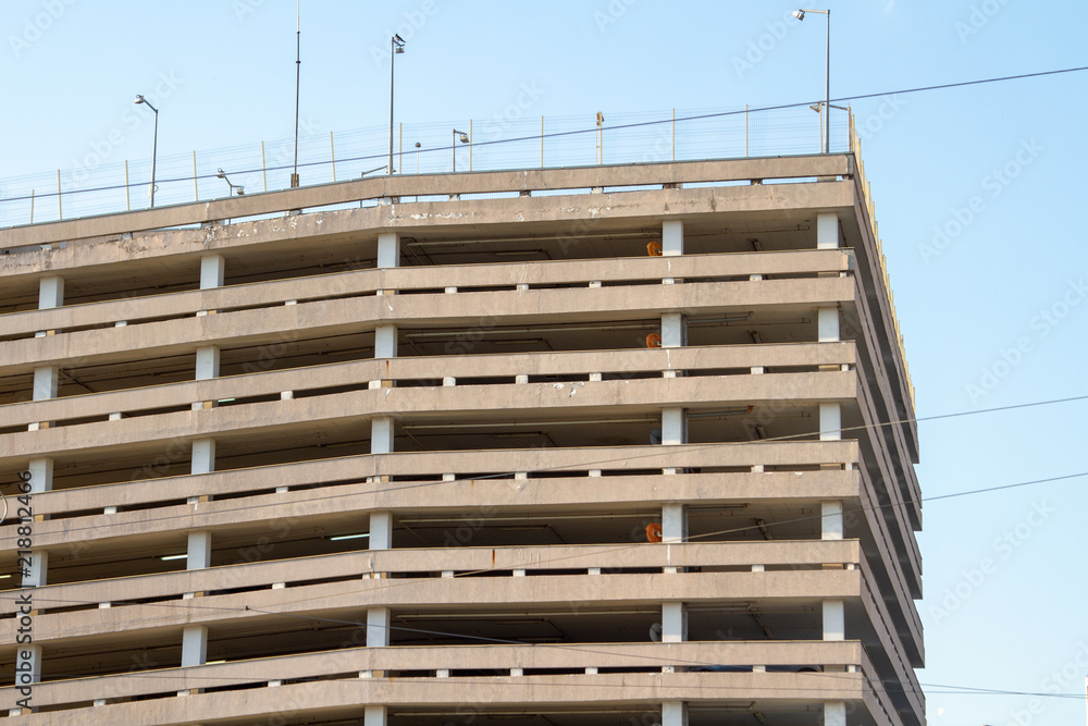 Multi-storey concrete parking with wires against the blue sky. Gray concrete overground parking. Multi-level city parking - an architectural solution against traffic jams in the city. Multi-storey concrete parking with wires against the blue sky. Gray concrete overground parking. Multi-level city parking - an architectural solution against traffic jams in the city.