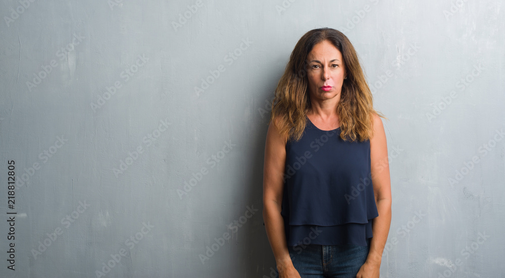 Middle age hispanic woman standing over grey grunge wall depressed and worry for distress, crying angry and afraid. Sad expression.