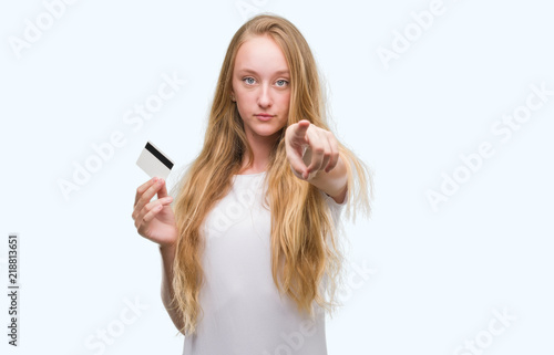 Blonde teenager woman holding credit card pointing with finger to the camera and to you, hand sign, positive and confident gesture from the front