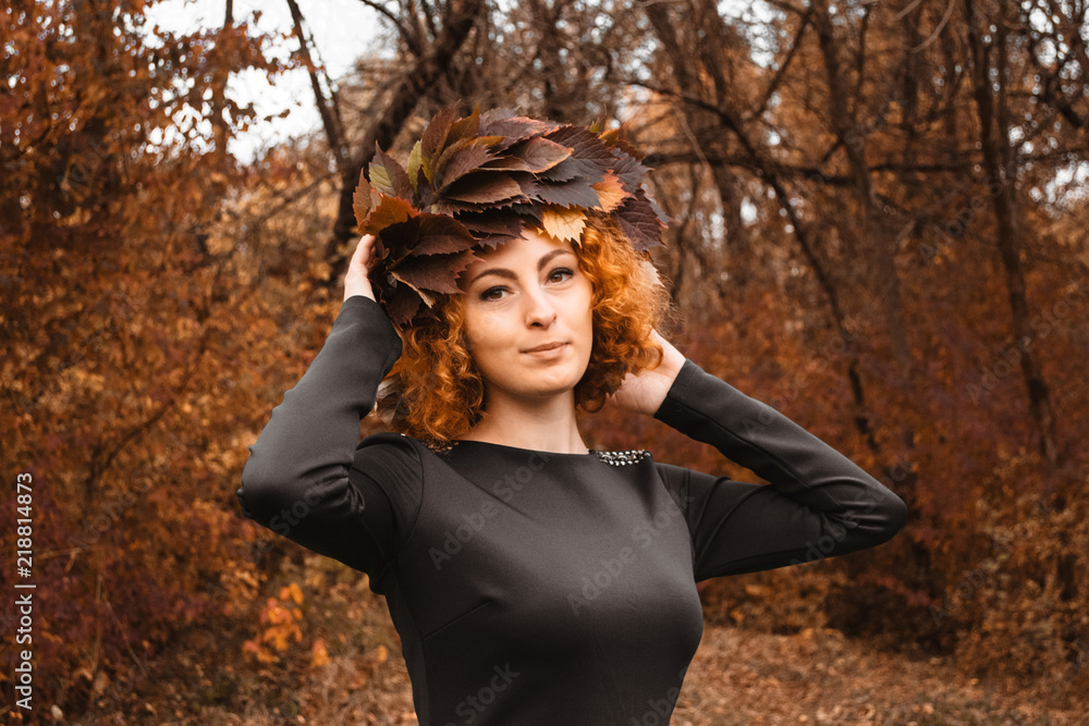 Redhead curly girl holding a wreath of grape leaves in a black dress. Young witch in the wood. Redhead curly girl holding a wreath of grape leaves in a black dress. Young witch in the wood.
