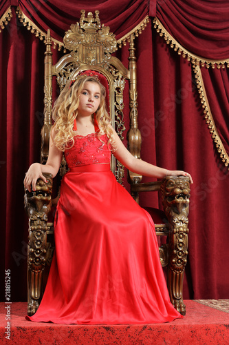 Blonde teenage girl in bright red dress sitting in vintage chair
