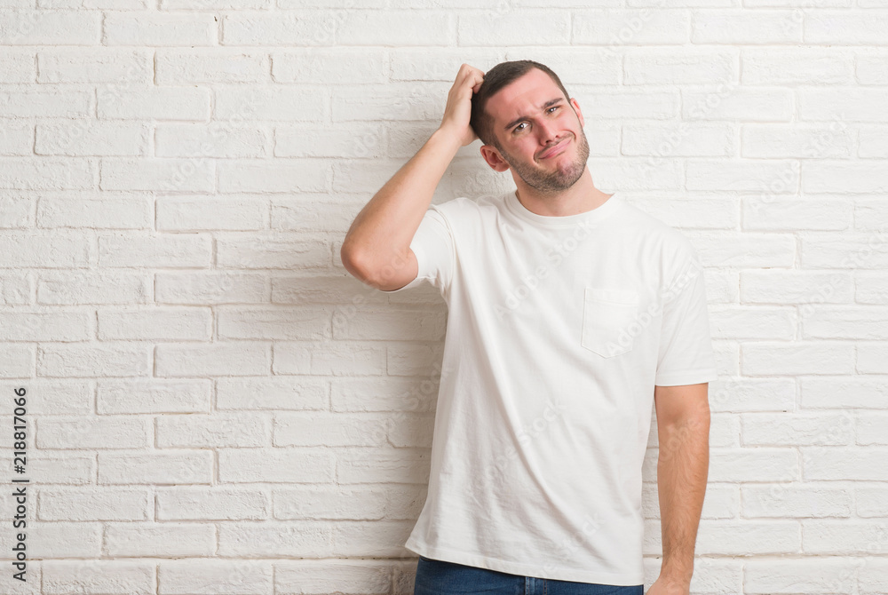 Young caucasian man standing over white brick wall doing happy thumbs up gesture with hand. Approving expression looking at the camera with showing success. Young caucasian man standing over white brick wall doing happy thumbs up gesture with hand. Approving expression looking at the camera with showing success.