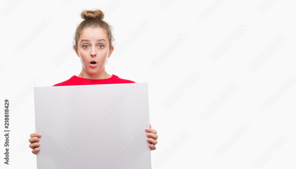 Young blonde woman holding advertising banner scared in shock with a surprise face, afraid and excited with fear expression Young blonde woman holding advertising banner scared in shock with a surprise face, afraid and excited with fear expression