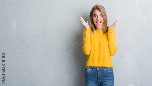 Beautiful young woman standing over grunge grey wall celebrating crazy and amazed for success with arms raised and open eyes screaming excited. Winner concept