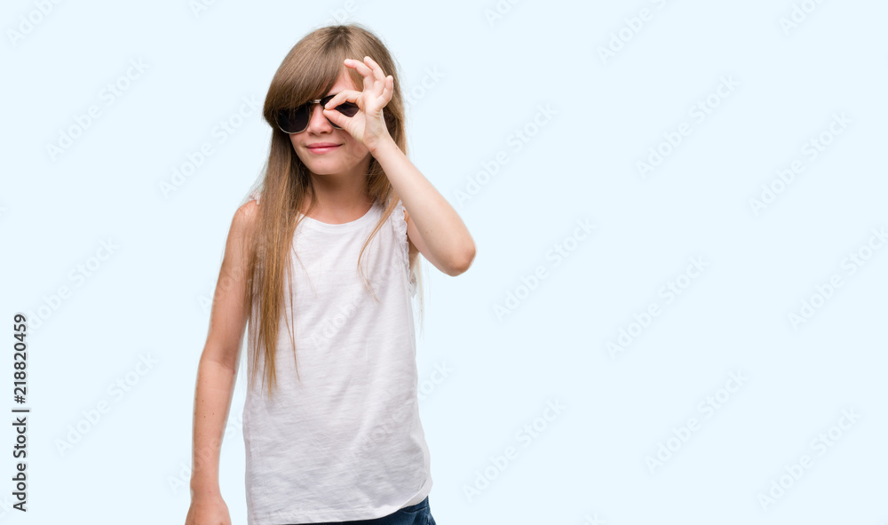 Young blonde toddler wearing sunglasses with happy face smiling doing ok sign with hand on eye looking through fingers Young blonde toddler wearing sunglasses with happy face smiling doing ok sign with hand on eye looking through fingers