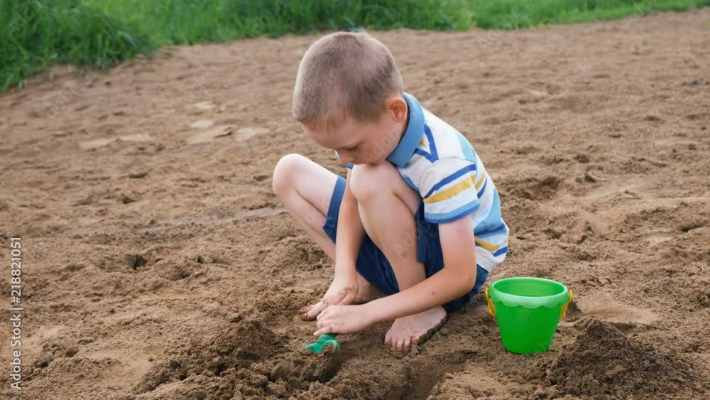 Serious little boy digs a pit with a shovel. Kid playing on the beach Serious little boy digs a pit with a shovel. Kid playing on the beach