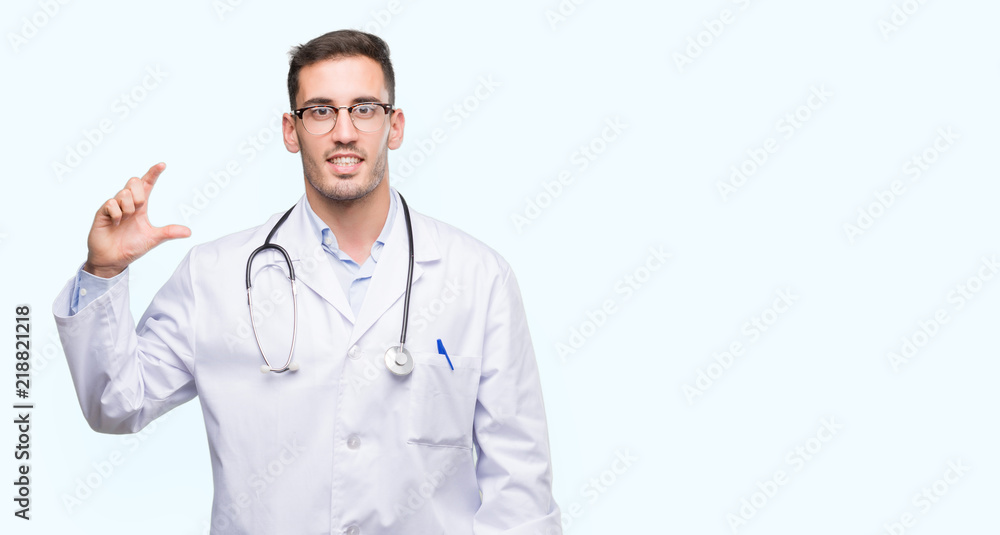 Handsome young doctor man smiling and confident gesturing with hand doing size sign with fingers while looking and the camera. Measure concept. Handsome young doctor man smiling and confident gesturing with hand doing size sign with fingers while looking and the camera. Measure concept.