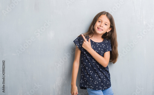 Young hispanic kid over grunge grey wall cheerful with a smile of face pointing with hand and finger up to the side with happy and natural expression on face looking at the camera.