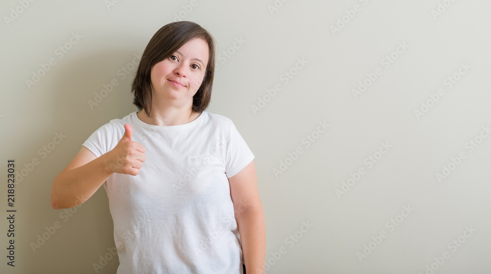 Down syndrome woman standing over wall doing happy thumbs up gesture with hand. Approving expression looking at the camera with showing success. Down syndrome woman standing over wall doing happy thumbs up gesture with hand. Approving expression looking at the camera with showing success.