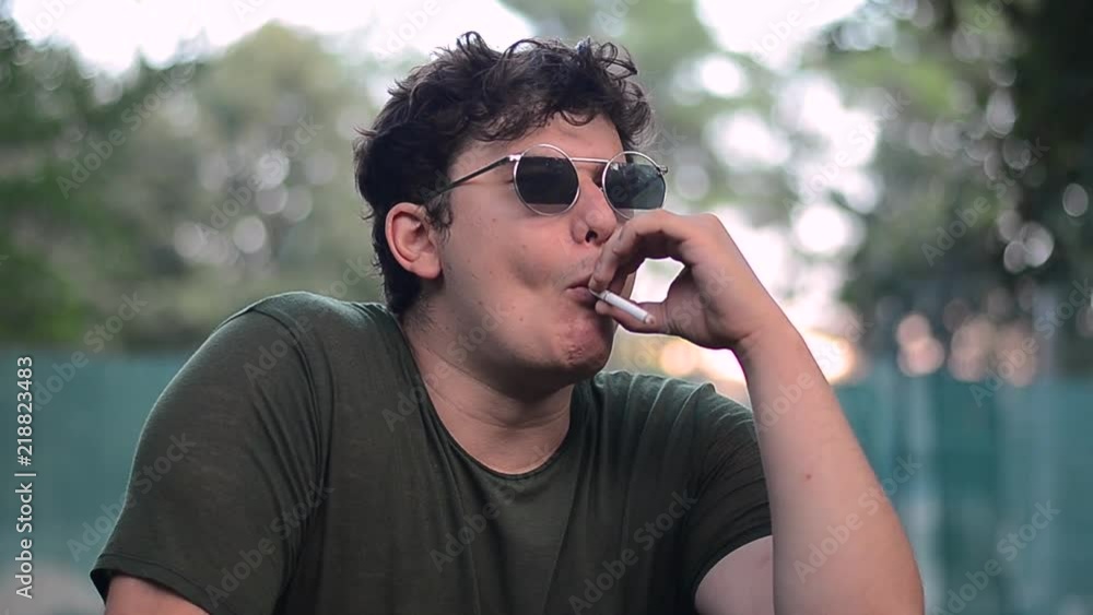 Young man having great time in park and smoking a cigarette. Young man having great time in park and smoking a cigarette.