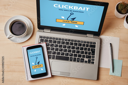 Clickbait concept on laptop and smartphone screen over wooden table. All screen content is designed by me. Flat lay
