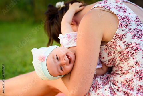 Mother holds infant baby girl and make her laugh to camera. on blanket in garden sunny summer day outdoors