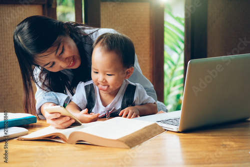 Business woman teaching her child about investment with multimedia and book, home school education. © BaracaPix