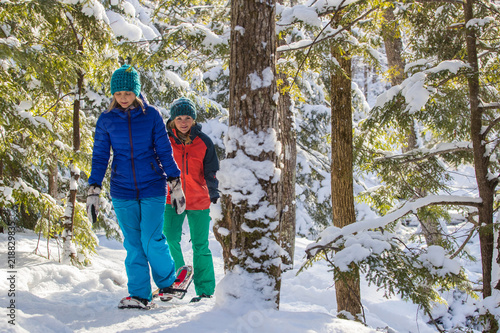 Pair of female friends snowshoeing in forest. photo