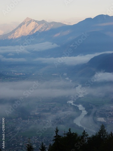 Alpine valley at dawn with winding Inn river and low clouds, trees in foreground and mountains in distance, Tyrol, Austria