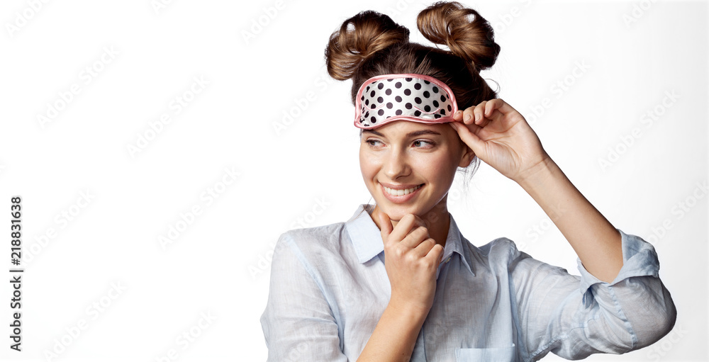 Cheerful smiling girl in sleeping mask on white background. Attractive funny female in stylish pajama standing and looking away.  - obrazy, fototapety, plakaty 