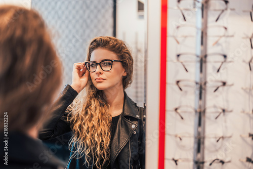 Woman trying new glasses, looking on mirror. photo