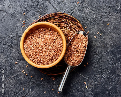 Fotografie Wild brown rice in wooden bowl on black background
