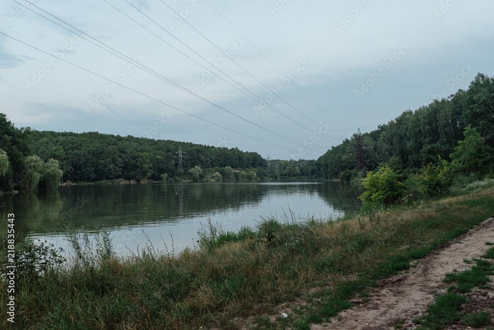 Obraz premium Wooden pier, platform. Trees on a lake shore in the evening. Forest lake. Vegetation by the lake. Sunset on the pond. Water resources of the planet, ecology.
