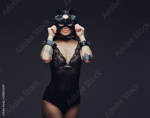 Sexy woman wearing black lingerie in BDSM cat leather mask and accessories posing on dark background. 