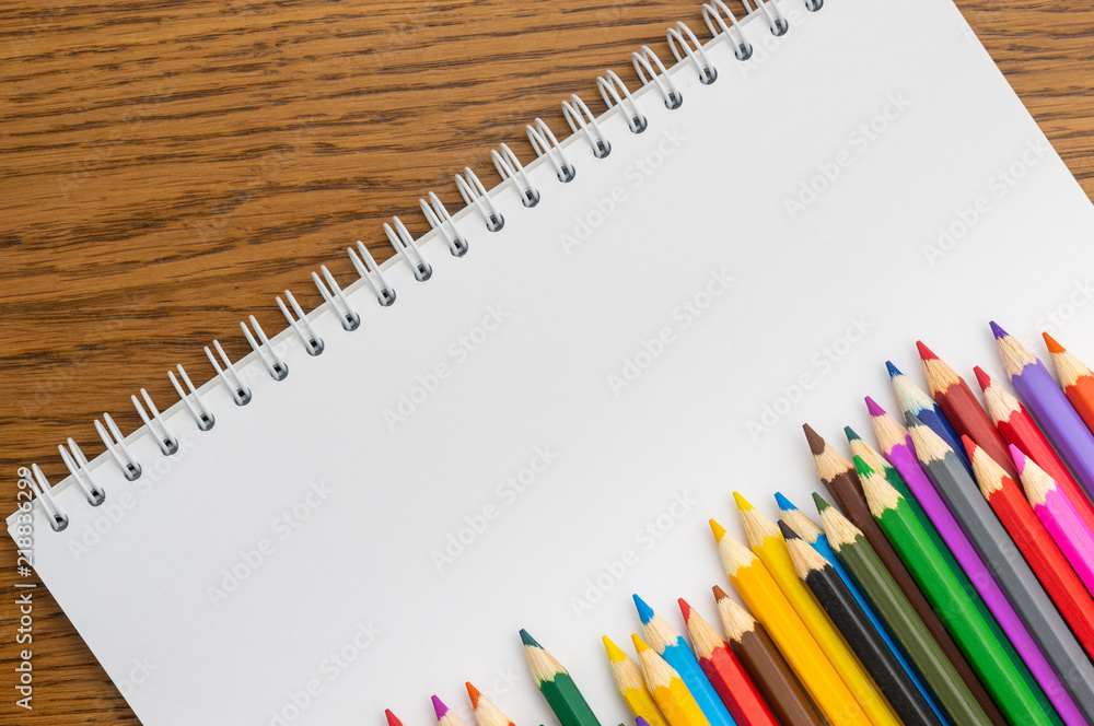 White paper and colored pencils lie on a wooden table White paper and colored pencils lie on a wooden table