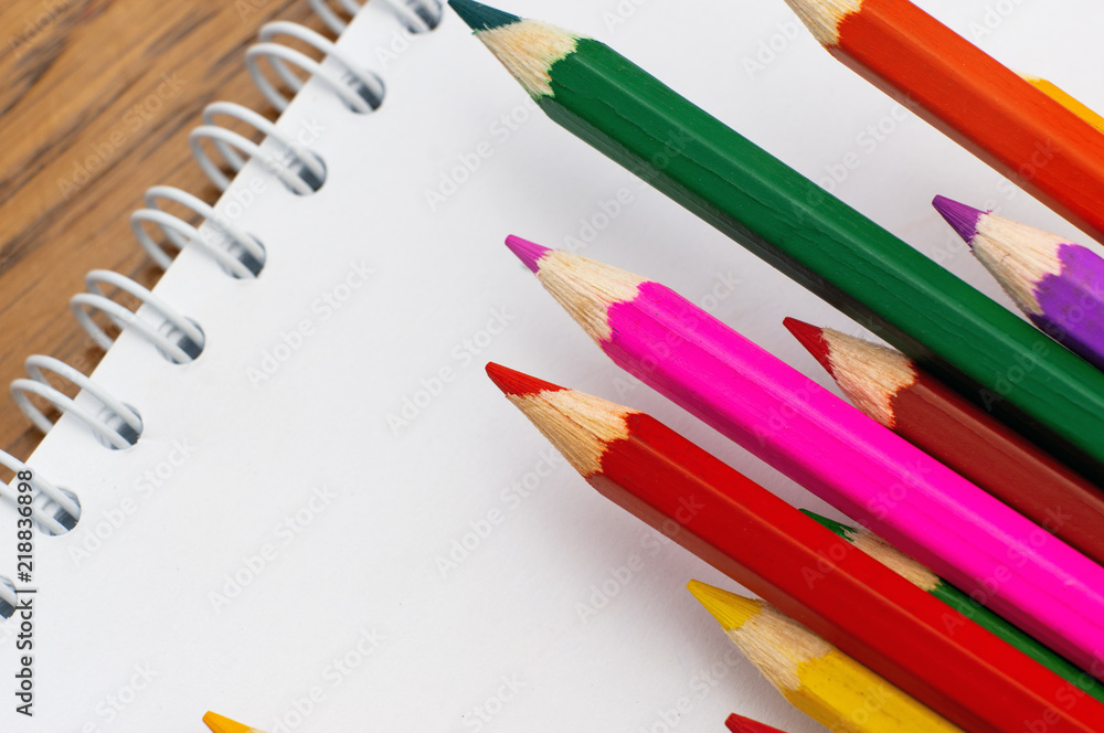 Fototapeta premium White paper and colored pencils lie on a wooden table
