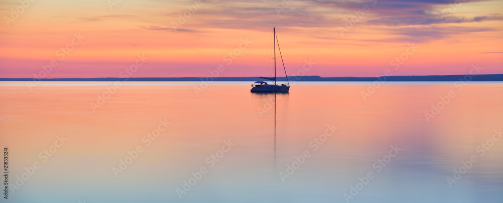 Fototapeta premium Świat w stanie spoczynku - żaglówka w spokojnym jeziorze o zachodzie słońca