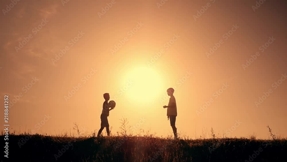 Two boys playing soccer at sunset. Silhouette of children playing with a ball at sunset. The concept of a happy family Two boys playing soccer at sunset. Silhouette of children playing with a ball at sunset. The concept of a happy family