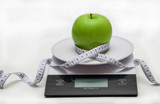 Green Apple on the scales and meter on white . The concept of weight loss and a healthy lifestyle.