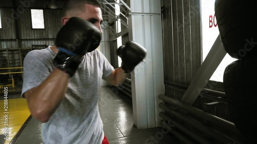 Male, caucasian boxer practicing kicks in black gloces using a puching bag made from car tyres. Old style boxing studio photo