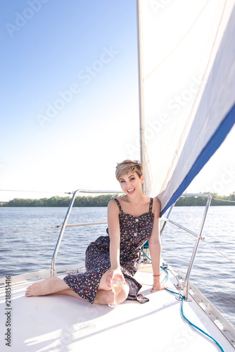 Happy beautiful woman in dress and a glass of wine, floating on a river on a yacht on a sunny day. Smiling woman on vacation, vacation at sea. Happy woman floating on a yacht by the sea