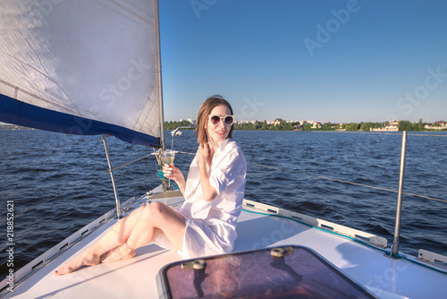 Portrait of a happy, attractive woman sailing on a yacht in the sunset with a glass of wine in her hands. Attractive woman resting on a ship with a glass of wine. Walk on the yacht by sea