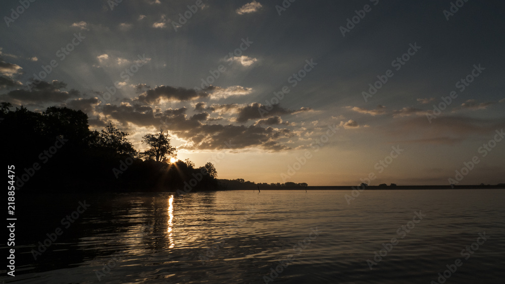 Sunrise with rays of sunshine through the clouds on a tranquil lake