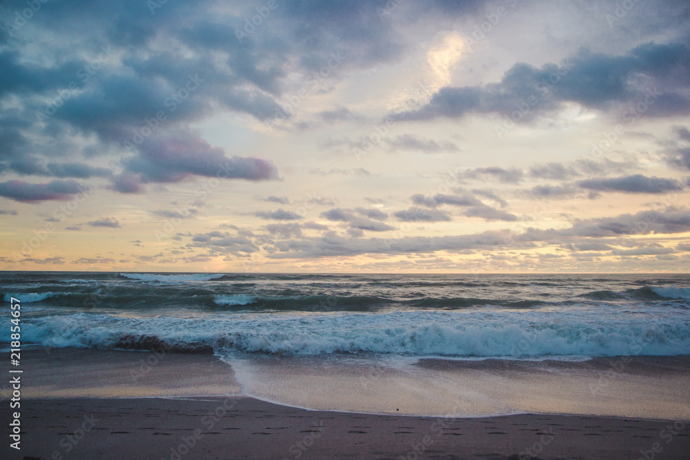 Fototapeta premium Horizon to shore waves at a cloudy, colourful sunset in Central America