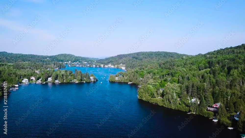 A pontoon boat travels through the lake's waterway into a larger body of water. It moves towards the camera. A pontoon boat travels through the lake's waterway into a larger body of water. It moves towards the camera.