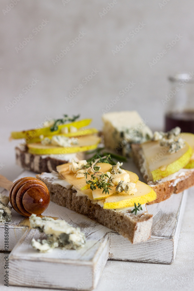Toast or bruschetta with ricotta or cream cheese, pear, honey and blue cheese on white wooden cutting board. Delicious breakfast or snack on a light background.