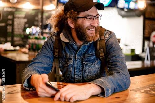 Bild auf Leinwand Hairy man traveler in a denim jacket with a backpack sitting at a table in a caf