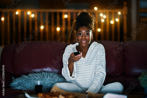 african american woman in pajamas staying up late at night eating pizza and watching tv