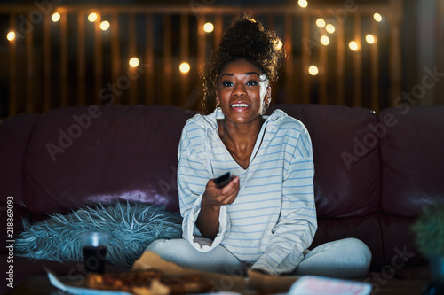 african american woman in pajamas staying up late at night eating pizza and watching tv