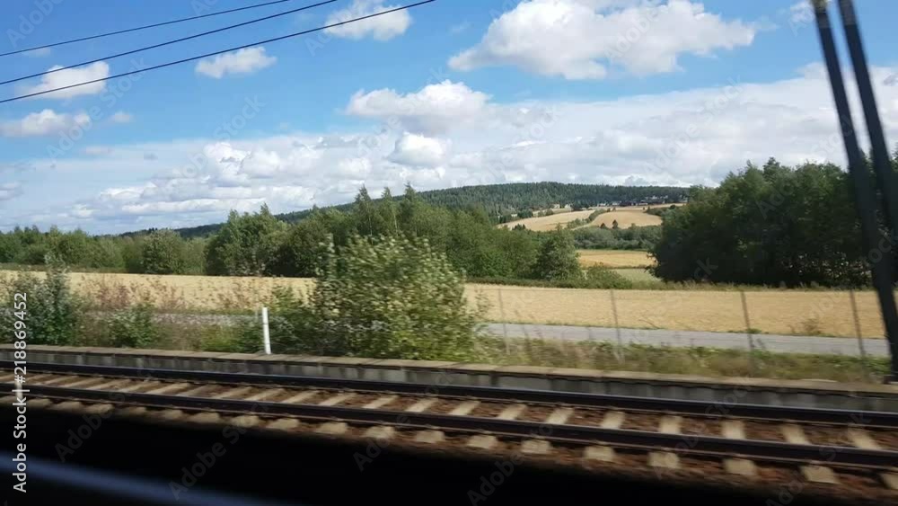 Filming out of a train window with a mobile phone. The sky is blue, and you can see a couple of farms in Norway.