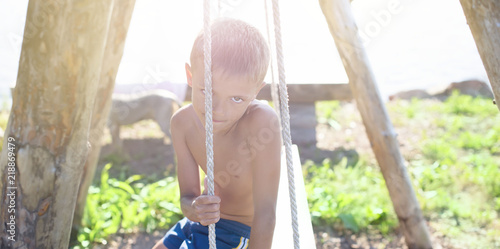 Defocus banner European boy sitting on a wooden old swing in a Park by the sea Holidays in the village games in nature