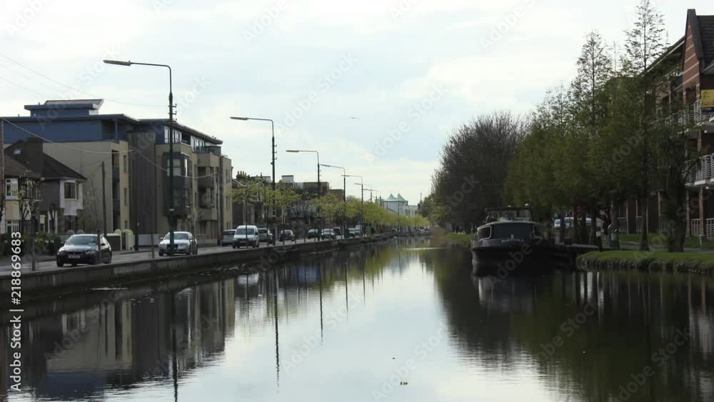 Timelapse of anchored boat on Dublin Grand Canal while people jog and cars are in traffic Timelapse of anchored boat on Dublin Grand Canal while people jog and cars are in traffic