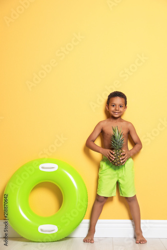 Cute African American boy with pineapple and bright inflatable ring near color wall