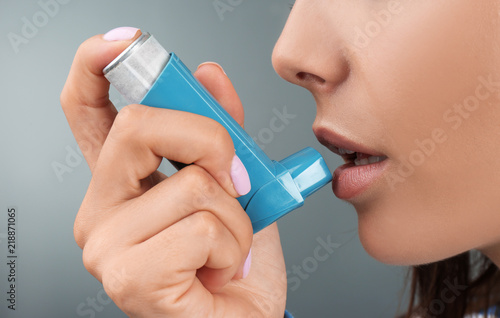 Young woman using asthma inhaler on color background, closeup photo