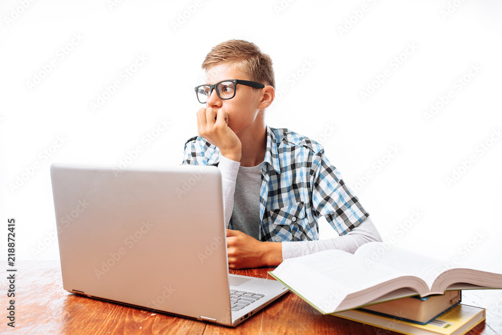 Young male student doing lessons with laptop and books sitting at table in Studio on white background Young male student doing lessons with laptop and books sitting at table in Studio on white background